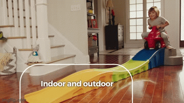 GIF of child model riding red scooter down a multi-colored ramp