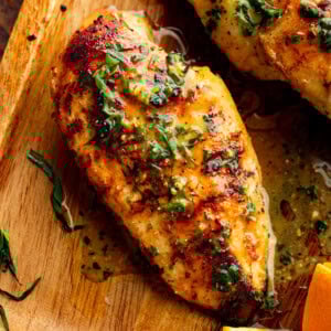 Grilled chicken breast on a wooden cutting board, topped with chopped fresh tarragon and a glossy citrus marinade.