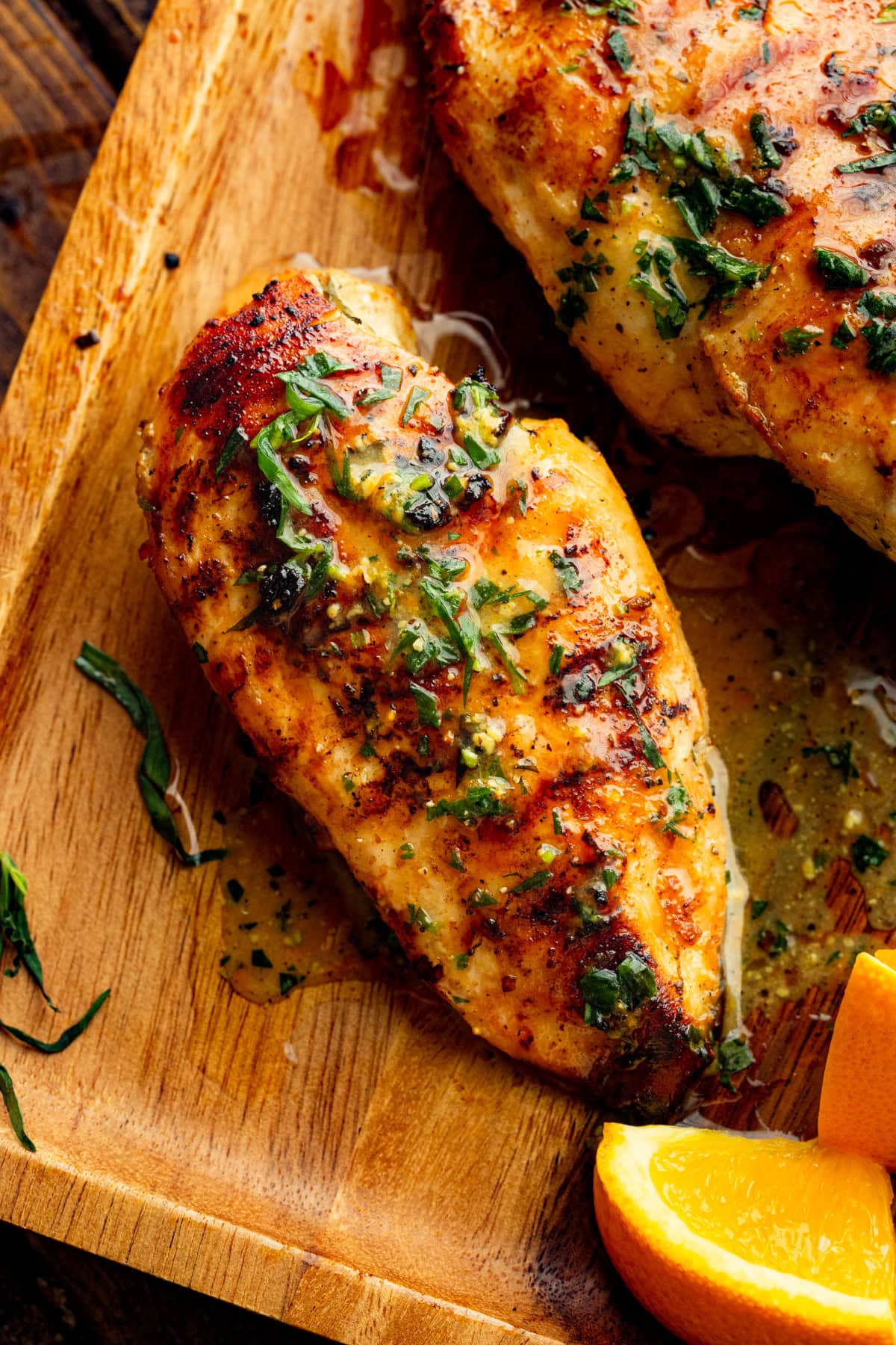 Whole grilled chicken breast resting beside a sliced half, both coated in citrus marinade and garnished with herbs.