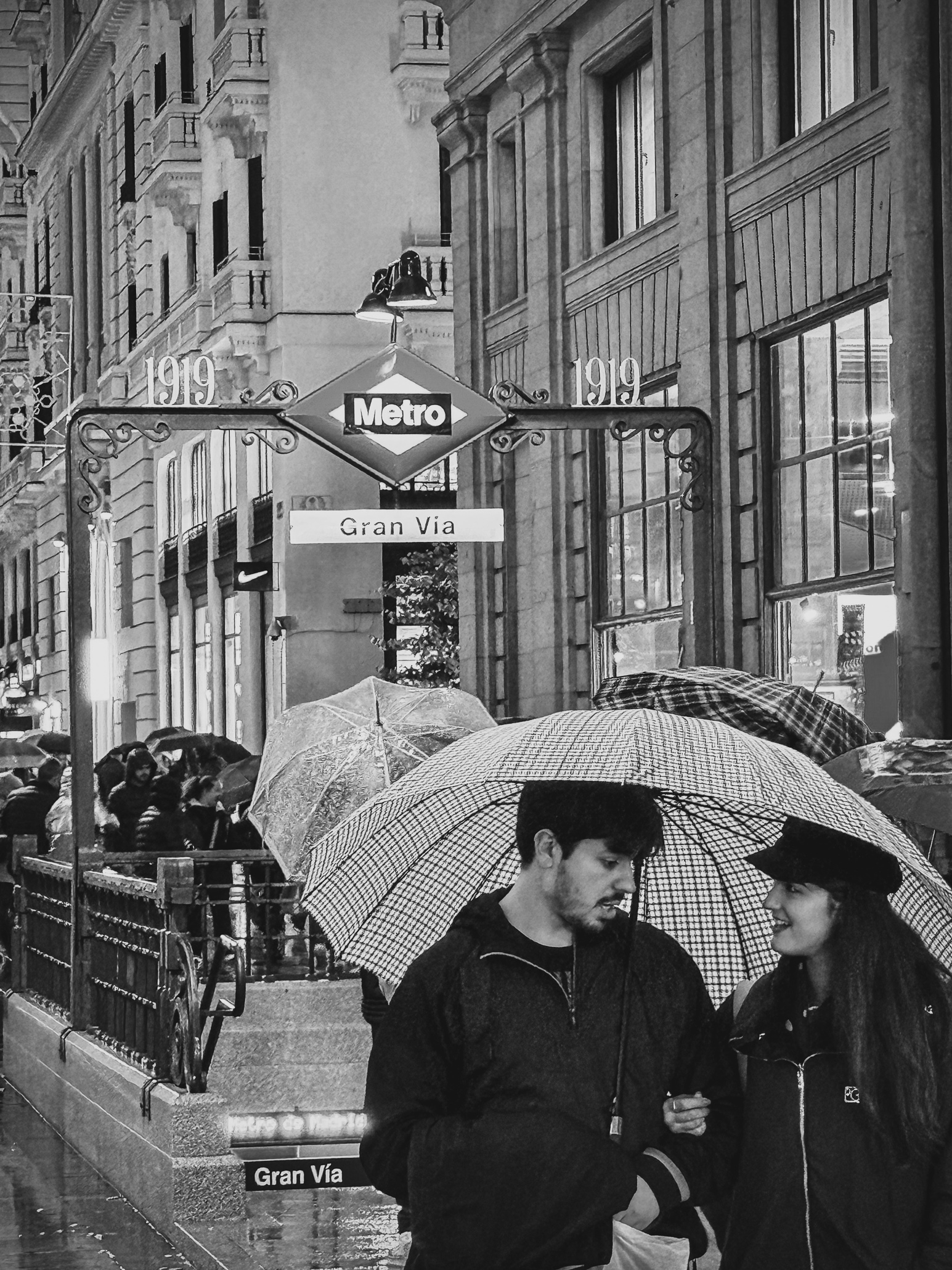 A young couple stepping into the rain under an umbrella with the girl smiling