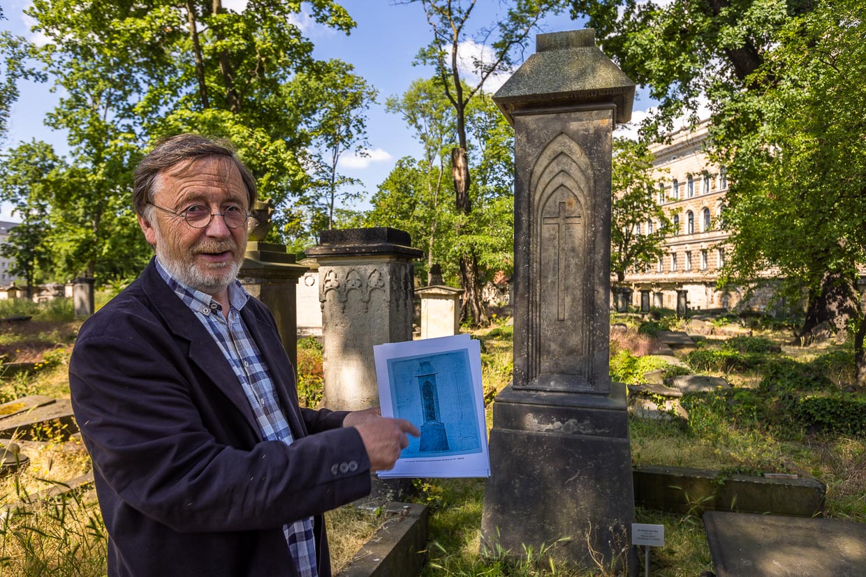 Volker Neumeister vom Förderverein Eliasfriedhof an einer Grabsäule nach dem Entwurf von Caspar David Friedrich. Hier das Grab von Dr Christian Ernst Ulrici, gstorben 1825. Volker Neumeister hält den Entwurf des Malers für ein Pfeilergrabmal mit Kreuz in gotischen Spitzbögen in der Hand / © Foto: Georg Berg