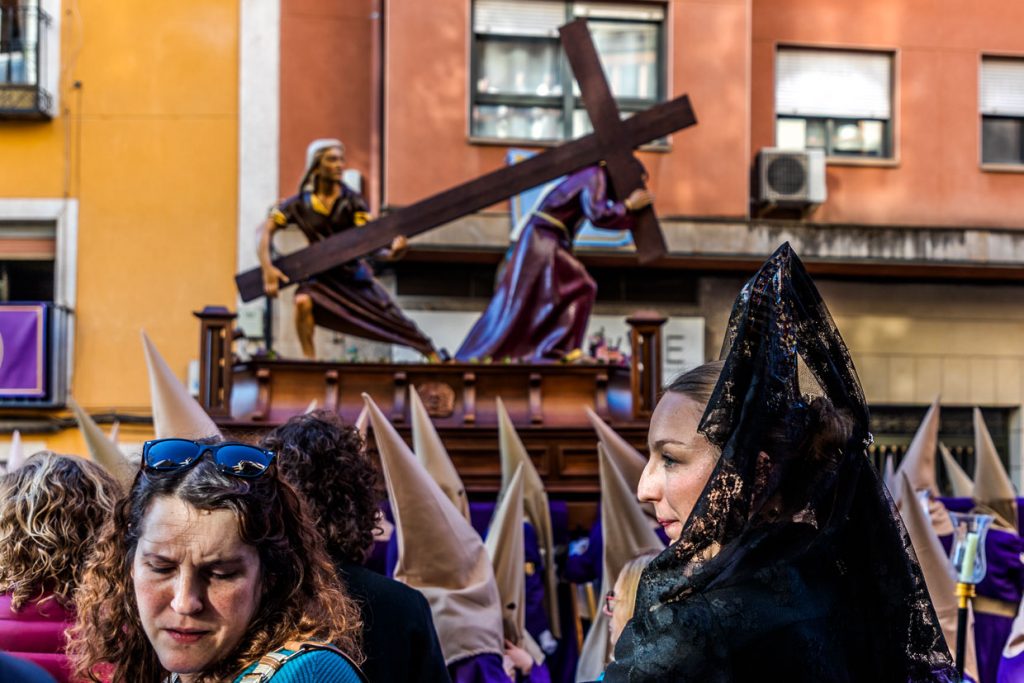 La Hermandad de Nuestro Padre Jesús Caído y La Verónica lleva el Paso del mismo nombre. Representa la escena en la que Jesús se desploma bajo el peso de la cruz camino de la crucifixión y Santa Verónica le entrega el sudario. Las mujeres de luto con velos y mantillas (manolas) muestran la conexión entre el acontecimiento bíblico y la vida actual: expresan la compasión y simpatía de la comunidad y crean un puente entre la tradición religiosa y la experiencia personal de dolor y esperanza / © Photo: Georg Berg