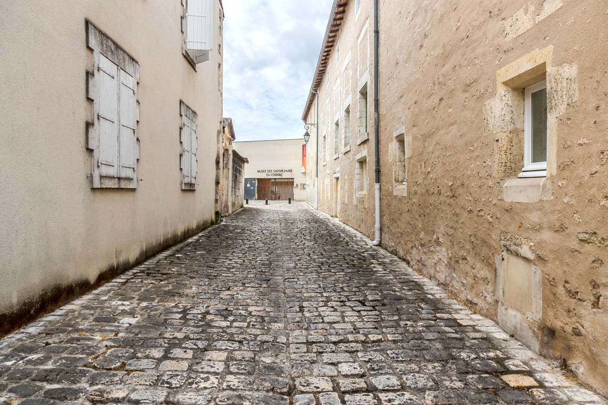Gasse in der Stadt Cognac mit Blick auf das „Musée des Arts du Cognac“. Es liegt zentral, zwischen der Innenstadt und der Hennessy-Brennerei, und bietet auf rund 2.000 m² einen umfassenden Einblick in die Geschichte, Kultur und Herstellung der berühmten Spirituose Cognac / © Foto: Georg Berg