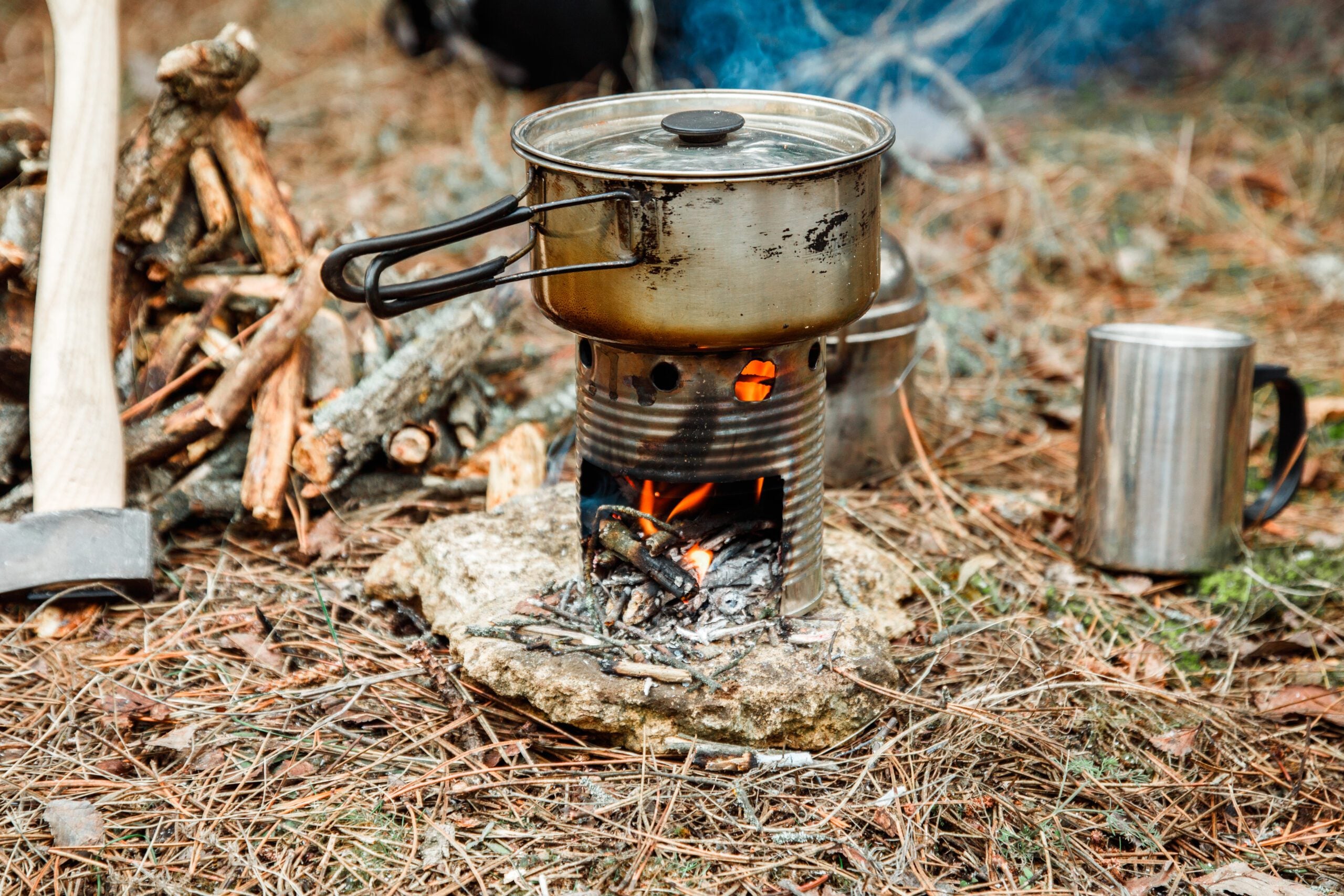 image: axe near a firewoods, camping diy woodstove, camping utensils and backpack on the background