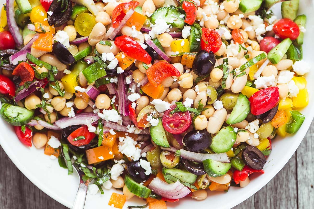 Mediterranean Bean Salad is the perfect no-mayo side salad for picnic and barbecue season, plus it makes fabulous healthy packable lunches! #7beansalad #nomayosalad #Laborday #summersalad #legumes #beans #picnic #potluck #Memorialday #4thofjuly #glutenfree #whole30 #recipe #easy #healthy #three #black #five #kidney #white Mediterranean Bean Salad in a white bowl.