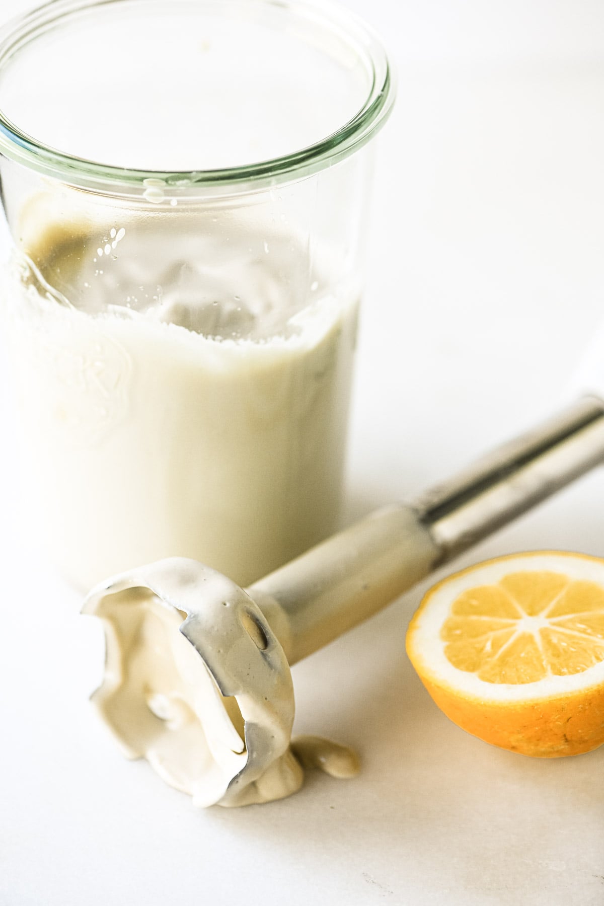 Whipped tahini in a glass jar, with immersion blender with cut lemon.
