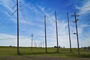 Power lines set against a vivid blue sky with farm fields in the foreground.
