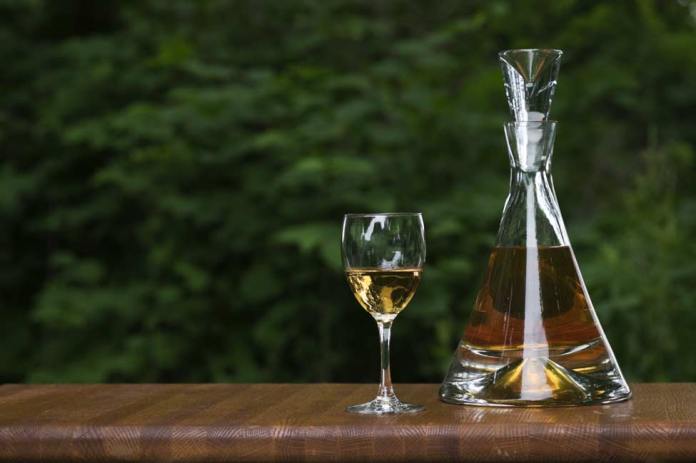 A snifter of Brandy with a decanter sitting on an oak table top.
