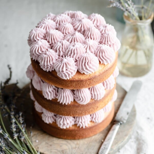 Three layered vanilla cake with purple frosting on a cutting board.