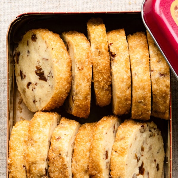 Baked pecan shortbread cookies with a sugar crust packed in a metal tin.