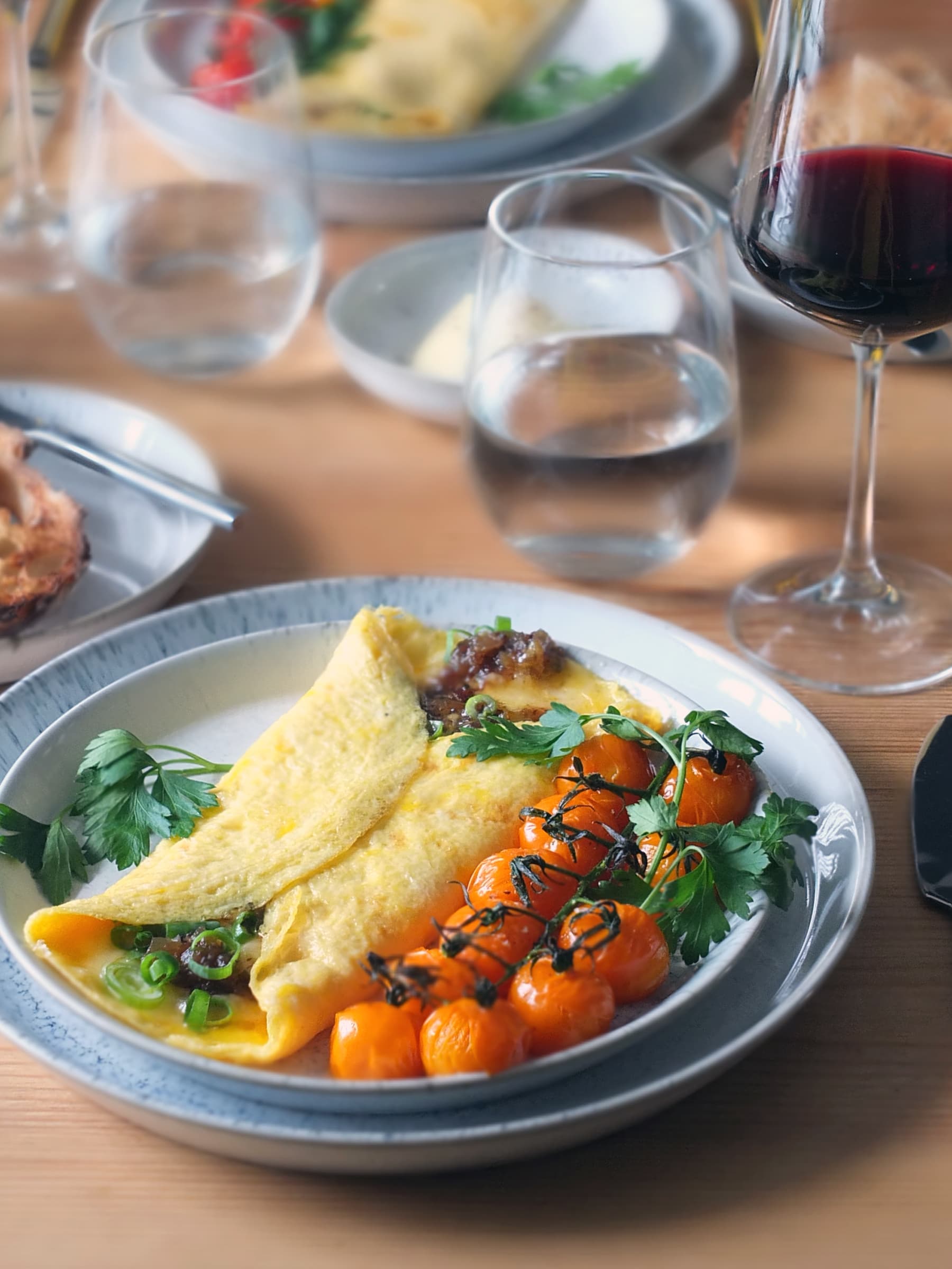 Close up image of a bacon jam and cheddar omelette on a plate with roasted cherry tomatoes on the side. There is a glass of merlot in the background.