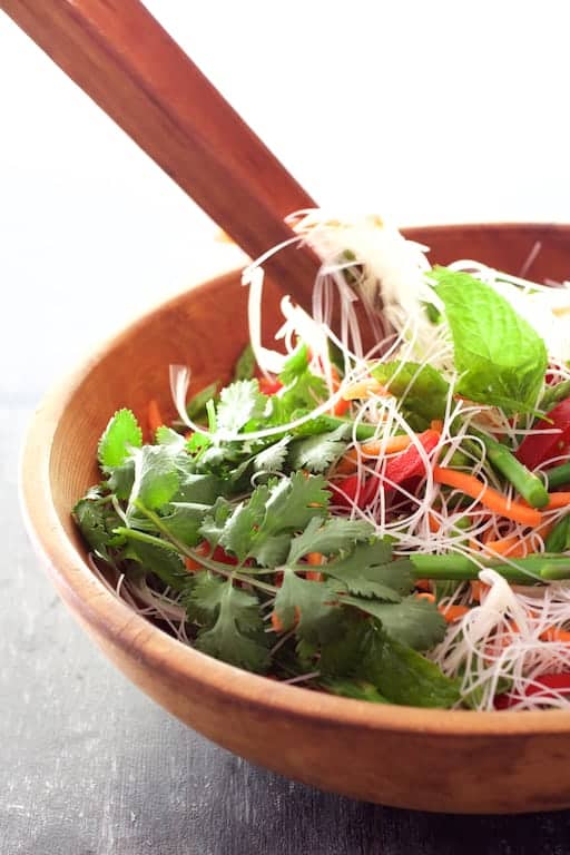 Photo of Vietnamese Spring Roll Salad being tossed together with wooden tongs in wooden bowl.