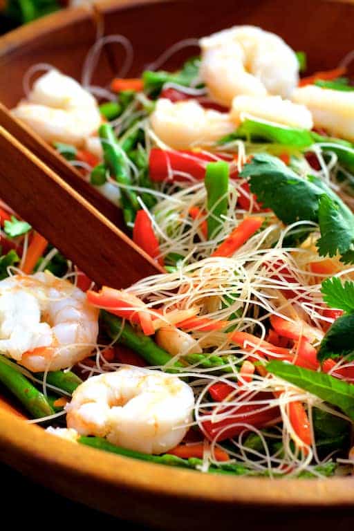 Photo of Vietnamese Spring Roll Salad being tossed together in wooden bowl with wooden tongs.
