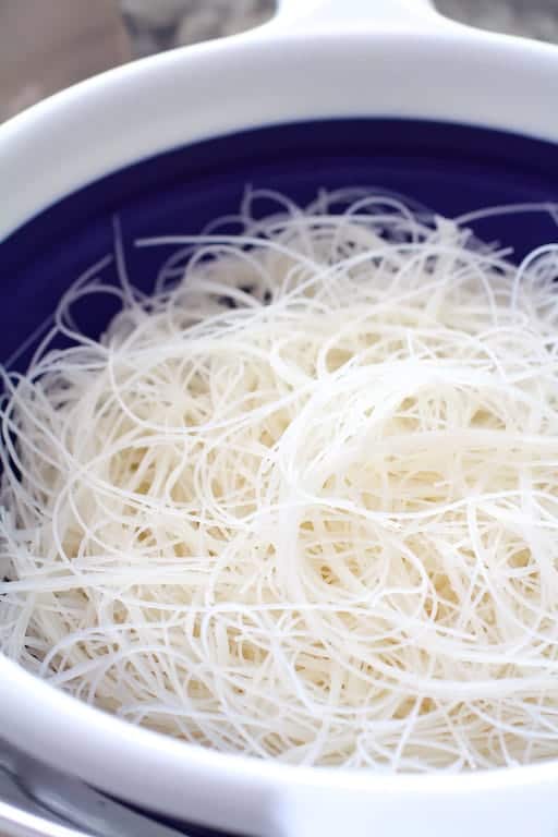 Photo of softened rice noodles in blue and white sieve.