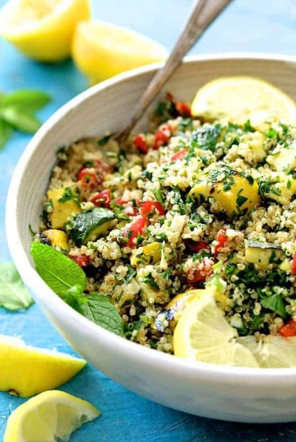 Quinoa Tabbouleh with Grilled Vegetables in white serving bowl garnished with fresh lemons.