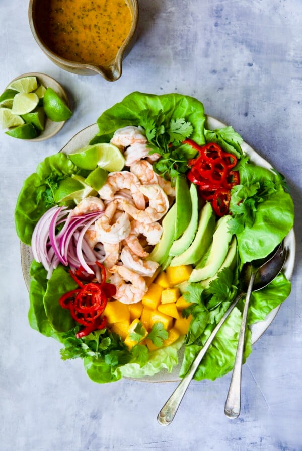 Butter Lettuce Salad with Shrimp, Mango and Avocado on round platter with serving utensils.