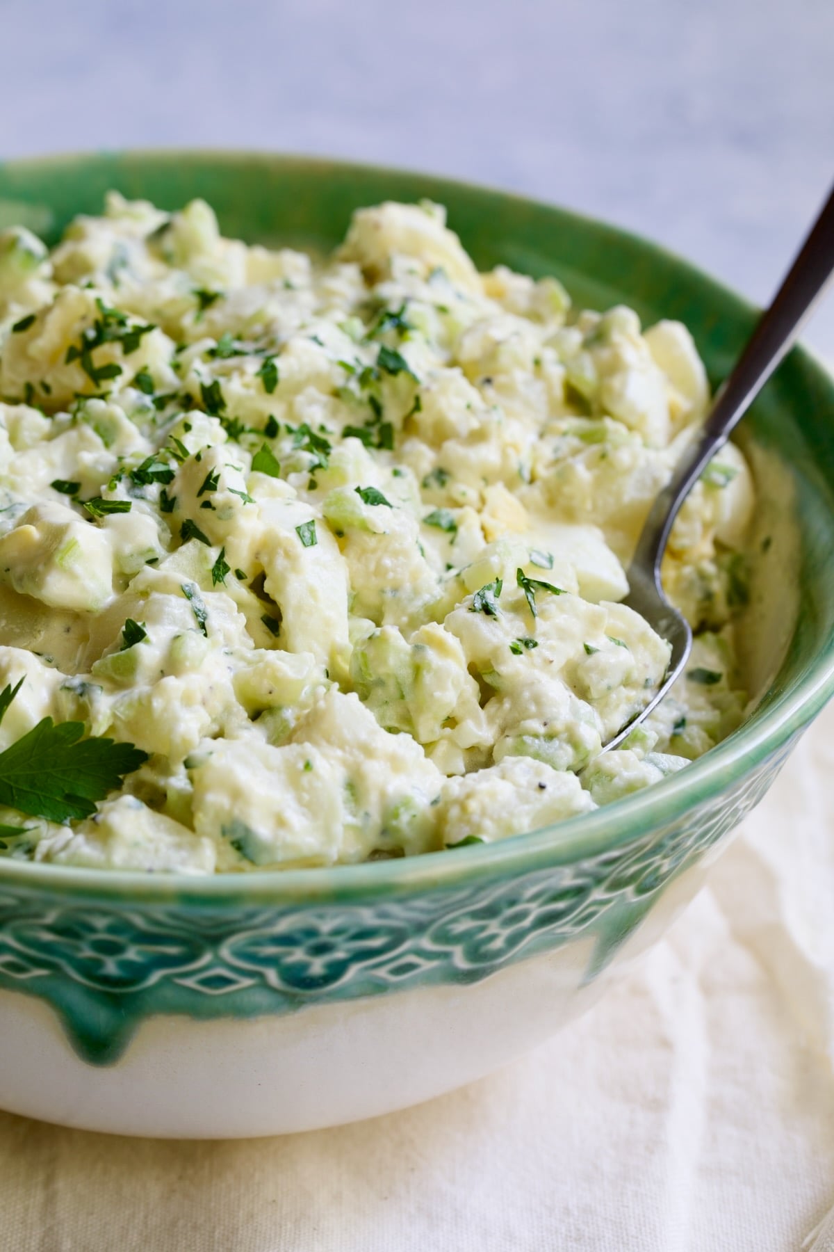Creamy Potato Cucumber Salad in green and white serving bowl with serving spoon.