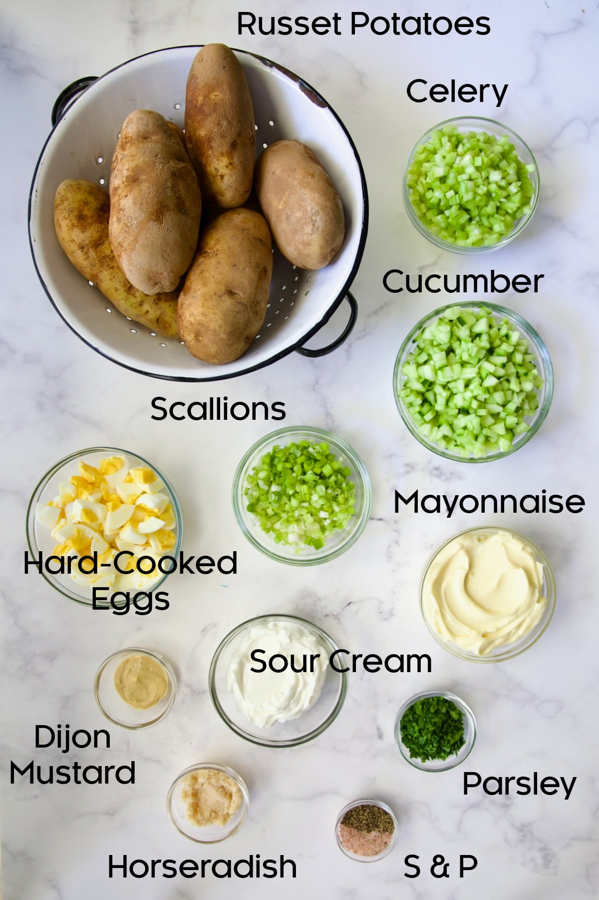 Ingredients for Creamy Potato Cucumber Salad in glass bowls on marble countertop.