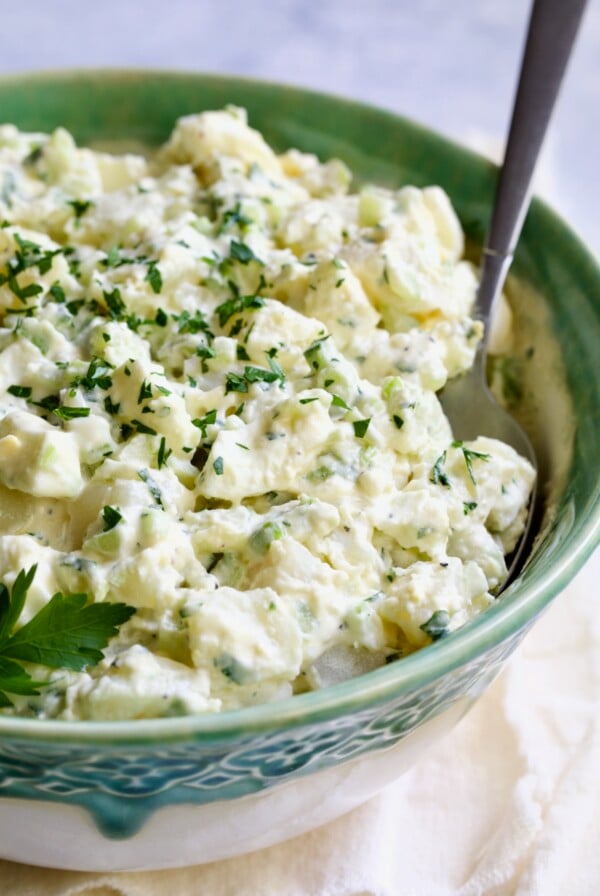 Creamy Potato Cucumber Salad in green and white serving bowl with serving spoon.