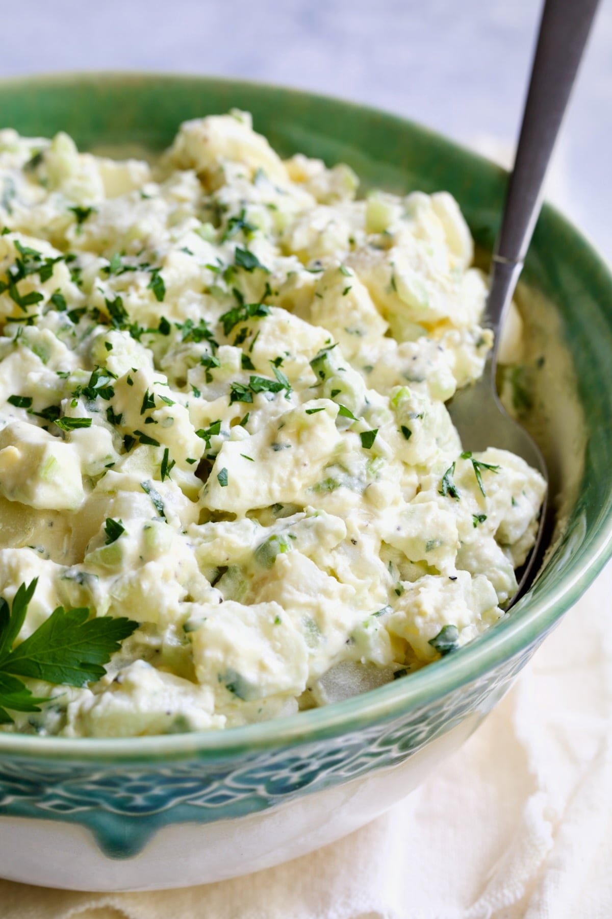 Creamy Potato Cucumber Salad in green and white serving bowl with serving spoon.