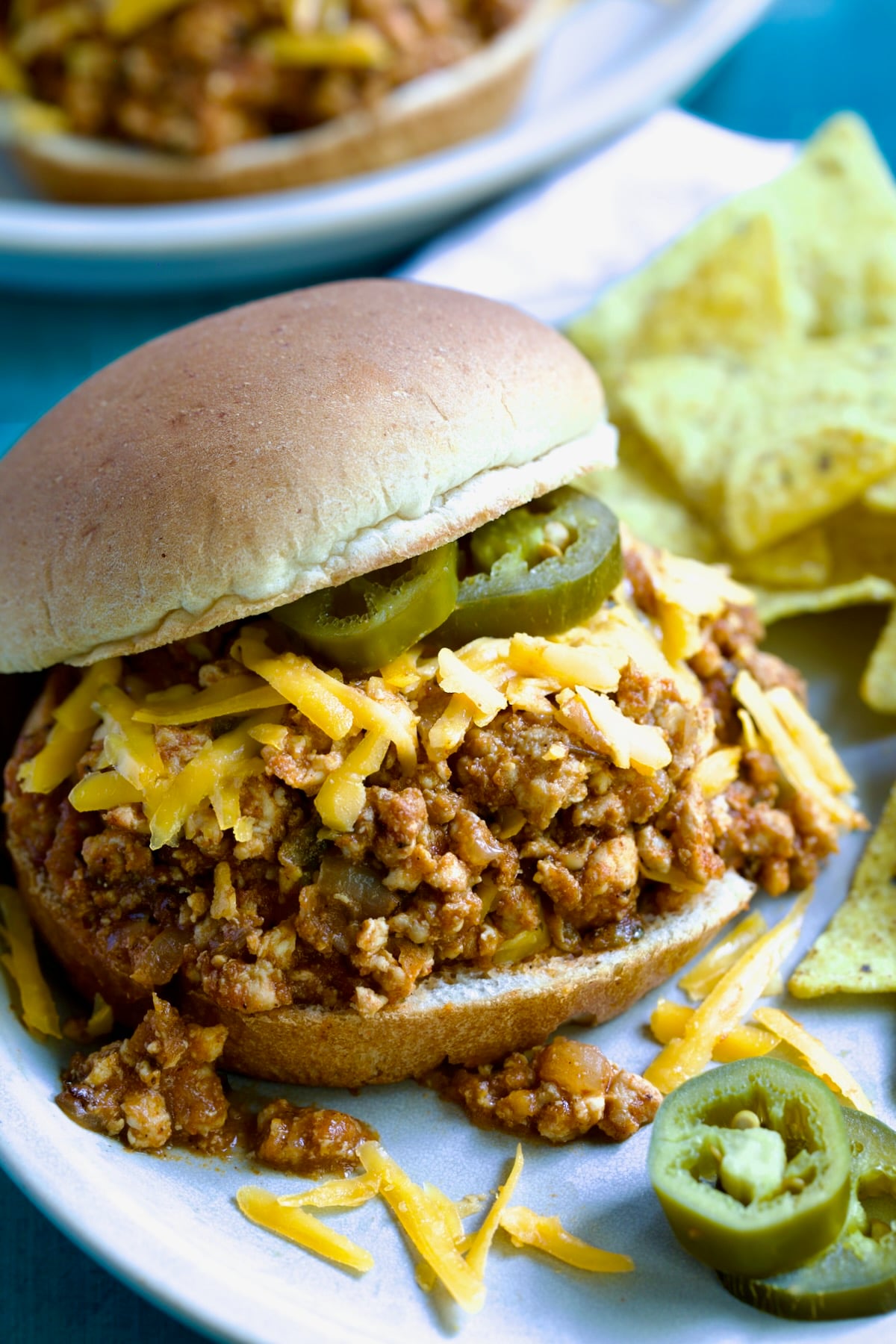 Chicken Sloppy Joes with grated cheddar cheese and jalapeno slices on top.