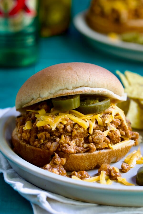 Chicken Sloppy Joes on plate with grated cheese and jalapeno slices.