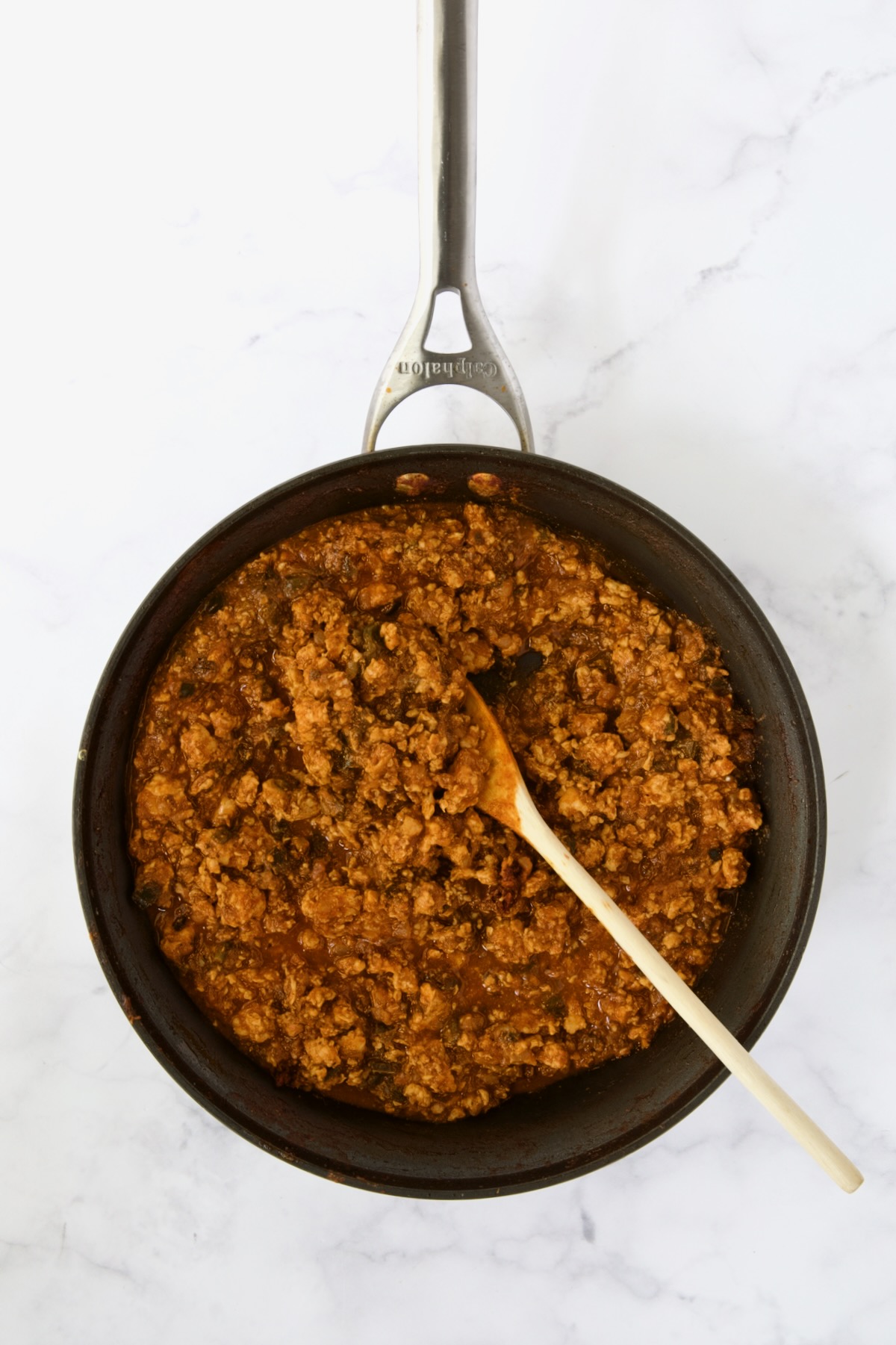 Ground chicken sloppy joes being stirred with wooden spoon in nonstick skillet.
