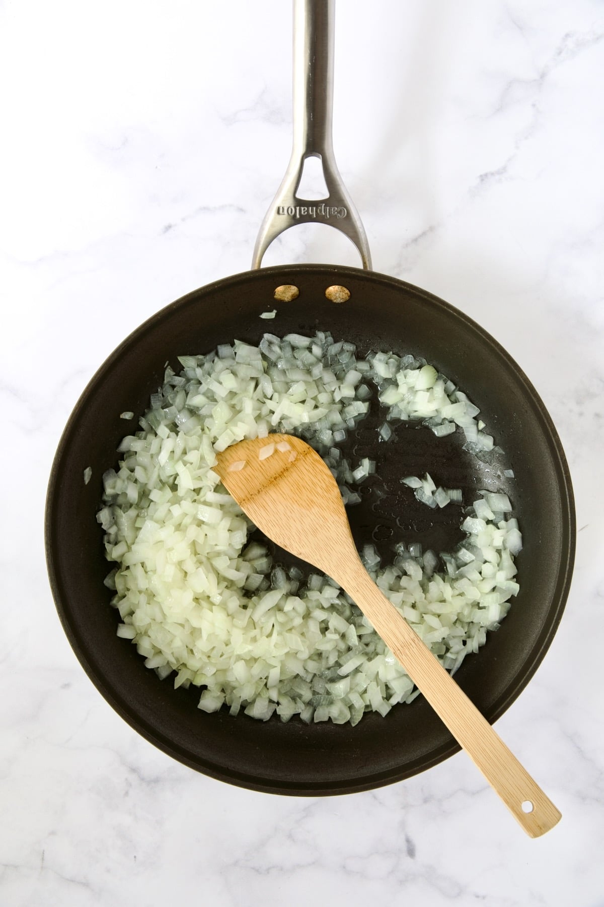 Cooked onions in nonstick pan being stirred with wooden spoon.