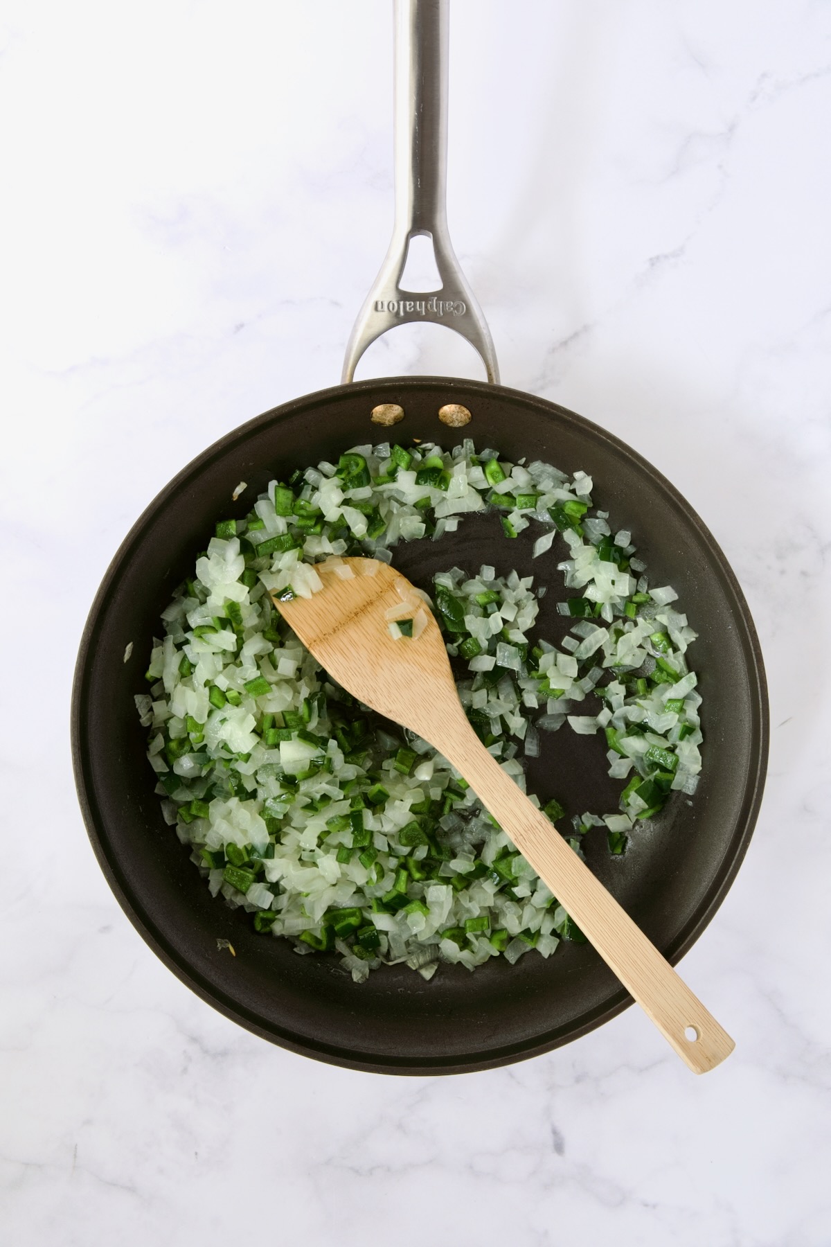 Cooked onions and poblano peppers in nonstick skillet being stirred with wooden spoon.