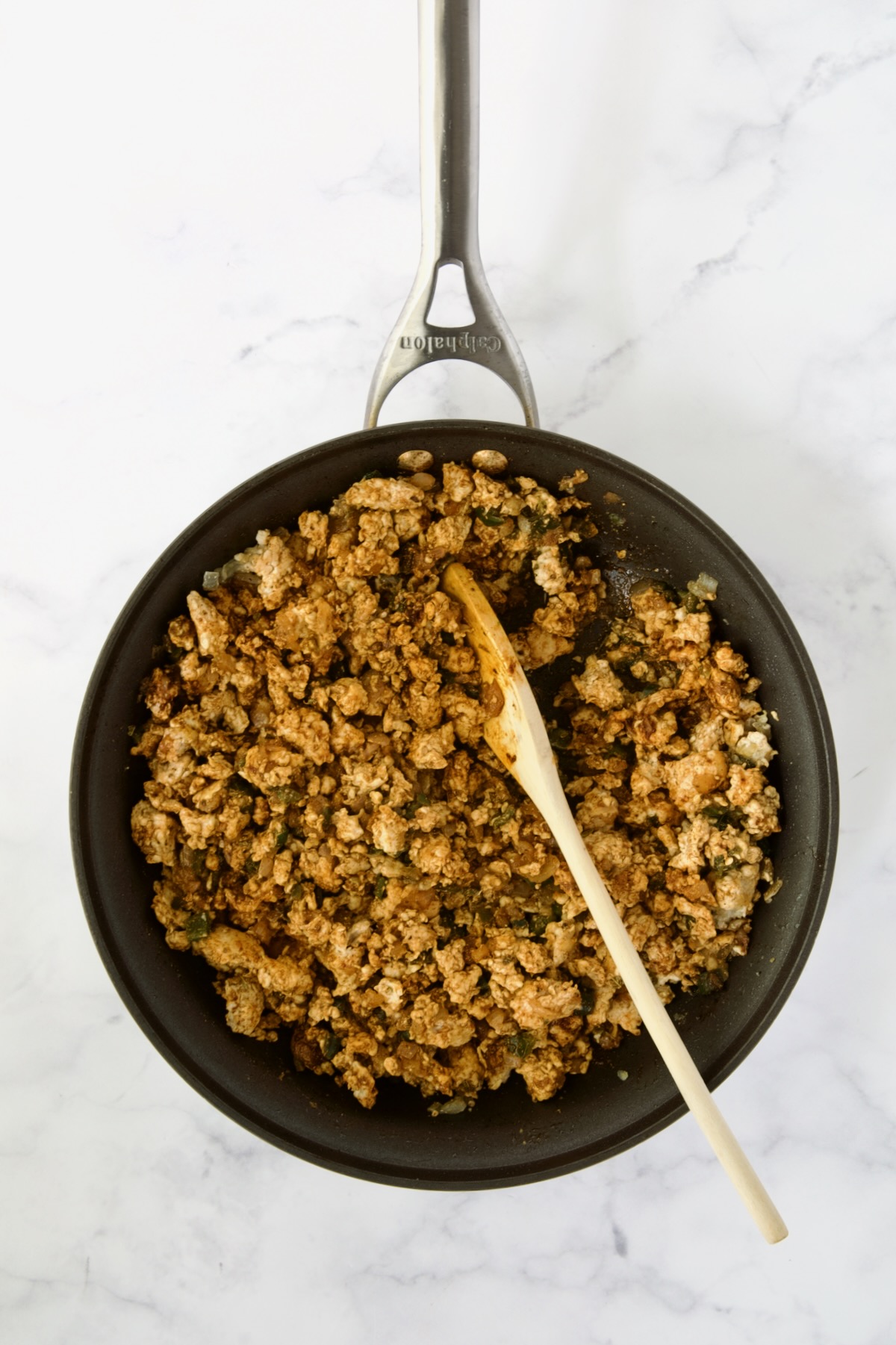 Cooked ground chicken with spices added being stirred with wooden spoon.