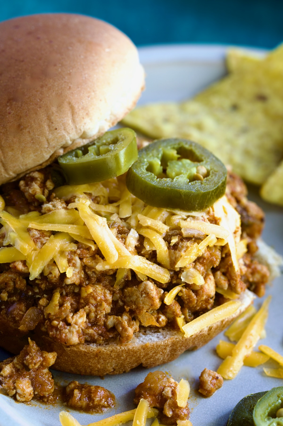 Chicken Sloppy Joes on bun with grated cheese and jalapeno slices on top.