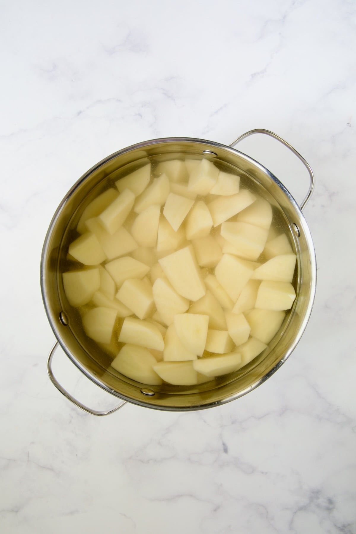 Peeled potatoes in water in stainless steel pot.