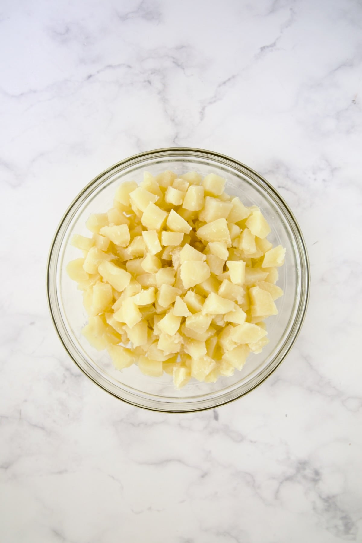 Cooked cubed potatoes in glass bowl.