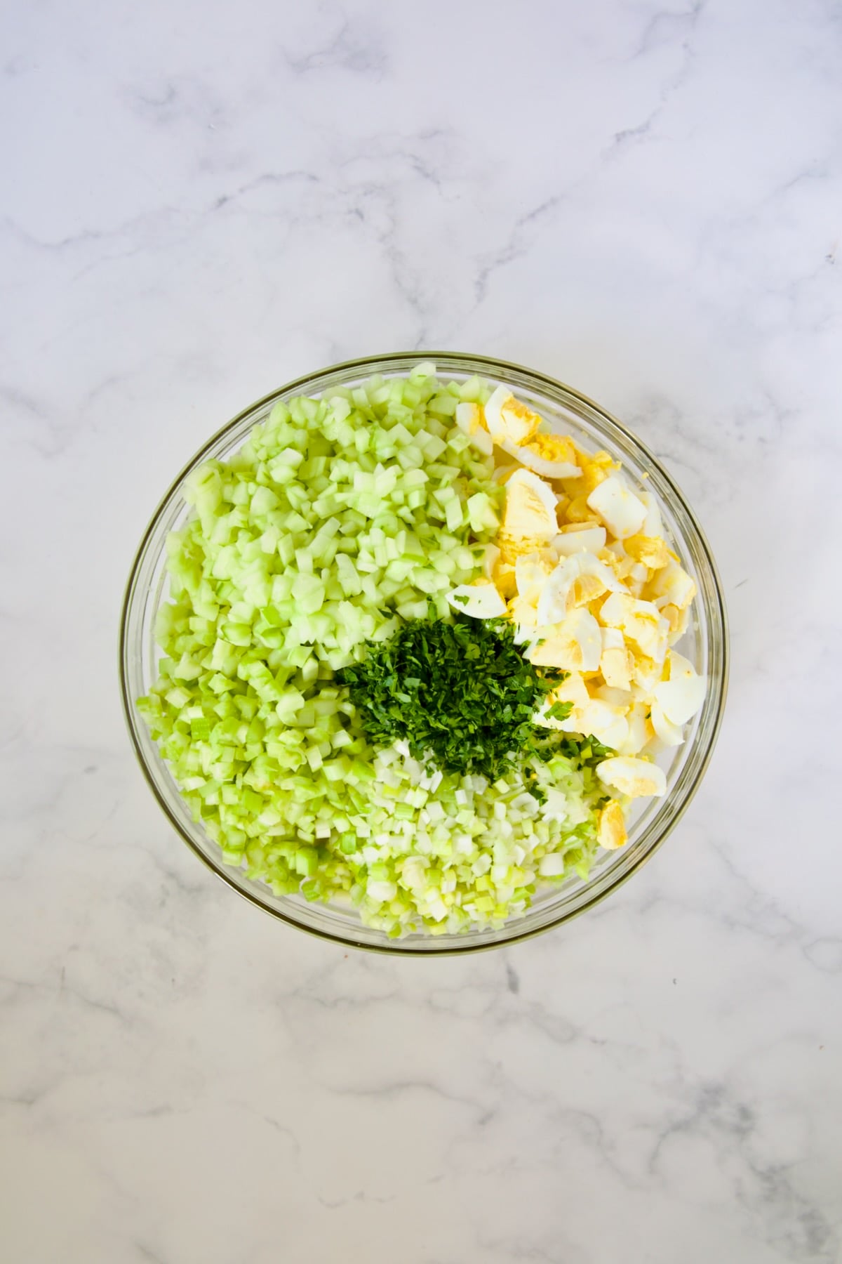 Hard-cooked eggs, celery, onions, cucumbers and parsley in glass bowl.