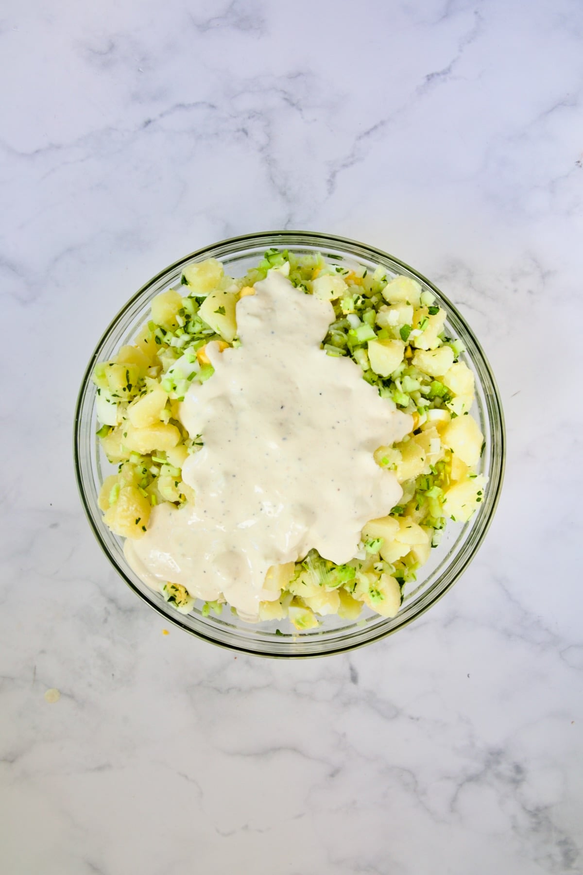 Dressing added to potato salad in glass bowl.
