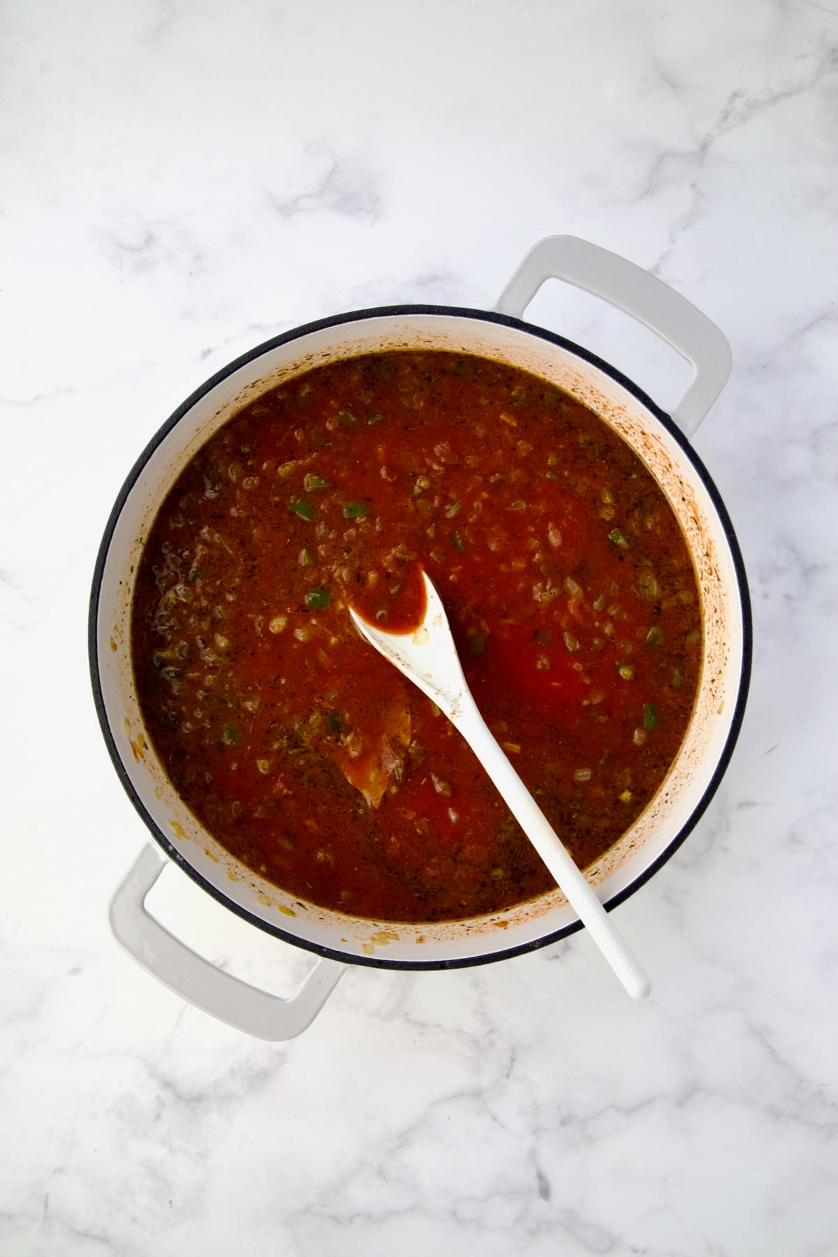 Tomato sauce and water added to vegetables and spices in white enamel cast iron skillet.