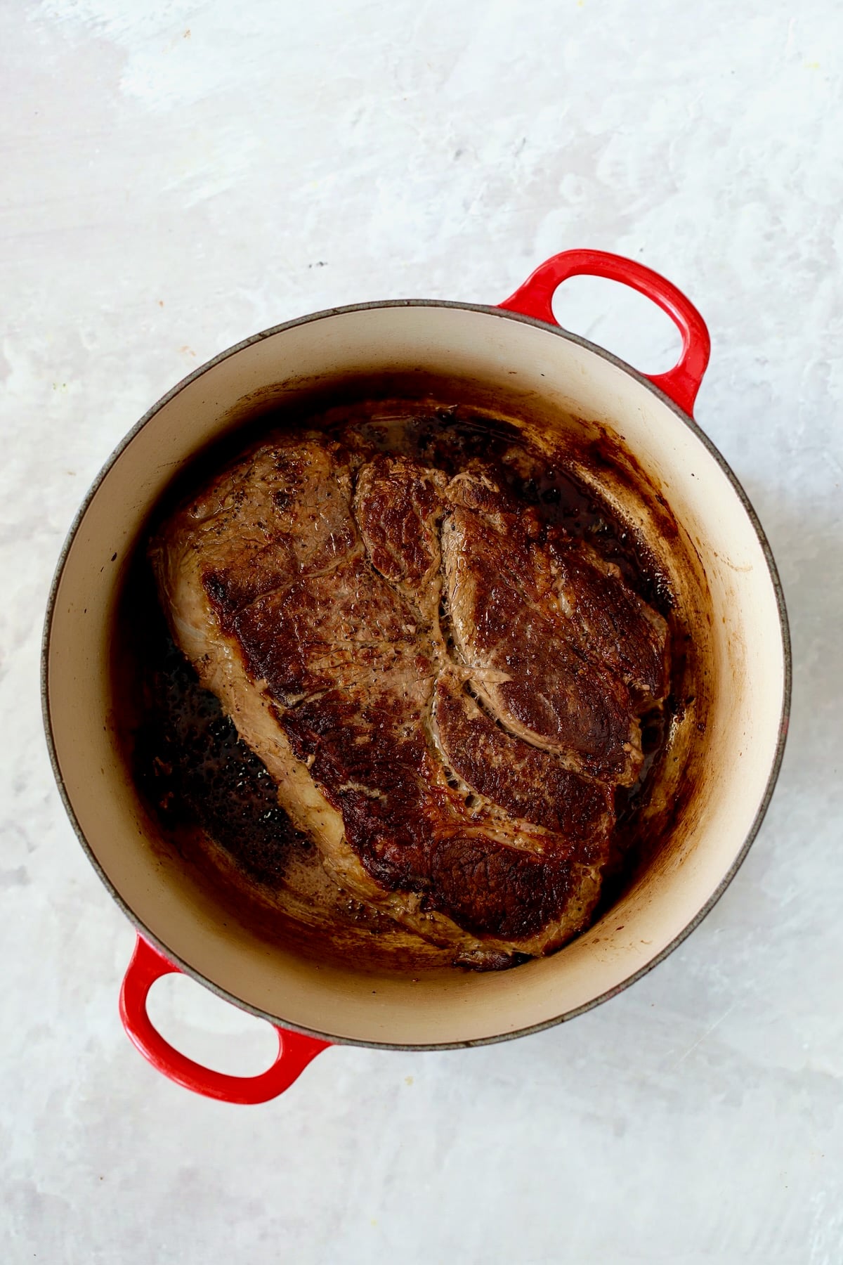Browned chuck roast in red enamel cast iron Dutch oven.