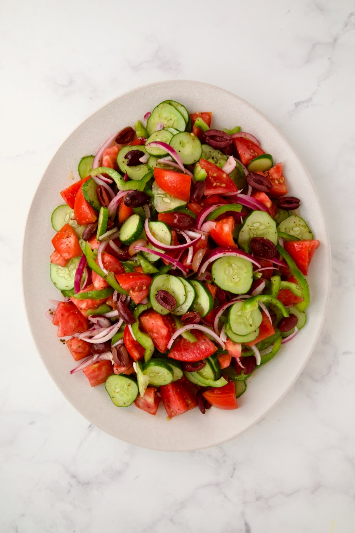 Greek salad on white oval platter before cheese is added.