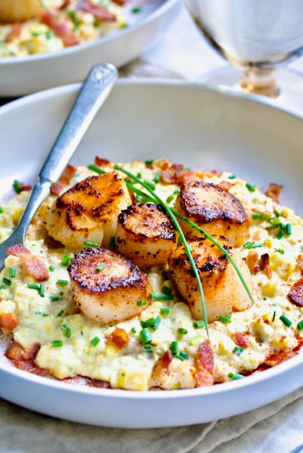 One serving of Seared Sea Scallops with Smoky Sweet Corn Puree on white plate with fork garnished with fresh chives.