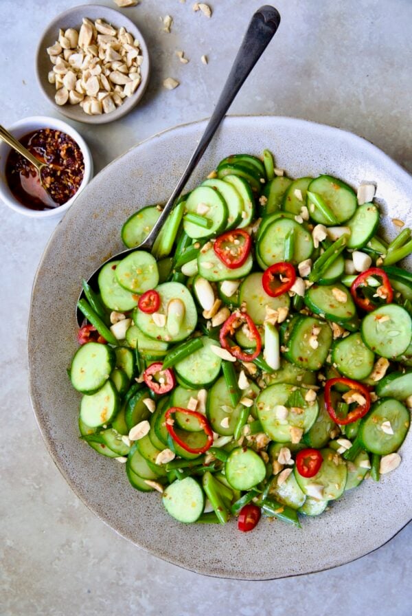 Spicy Asian Cucumber Salad in earthenware bowl with serving spoon garished with peanuts.