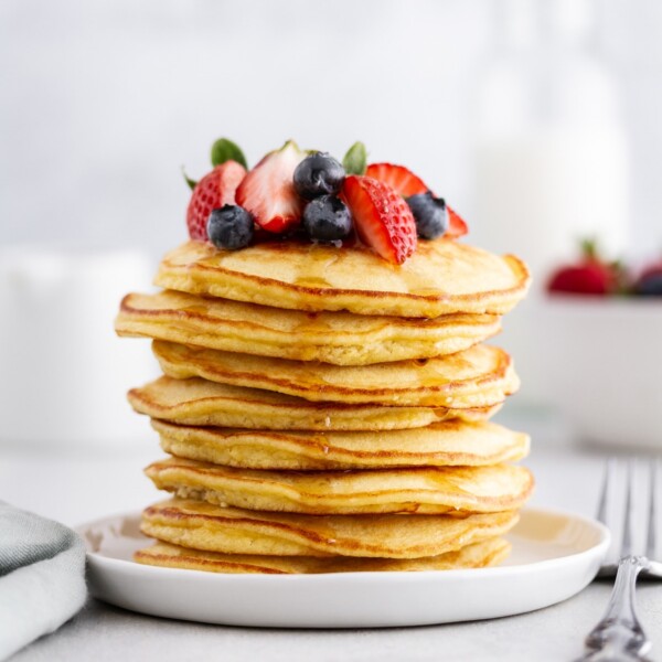 stack of coconut flour pancakes on a plate with berries on top.
