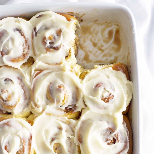 baked cinnamon rolls in white dish with cream cheese frosting.