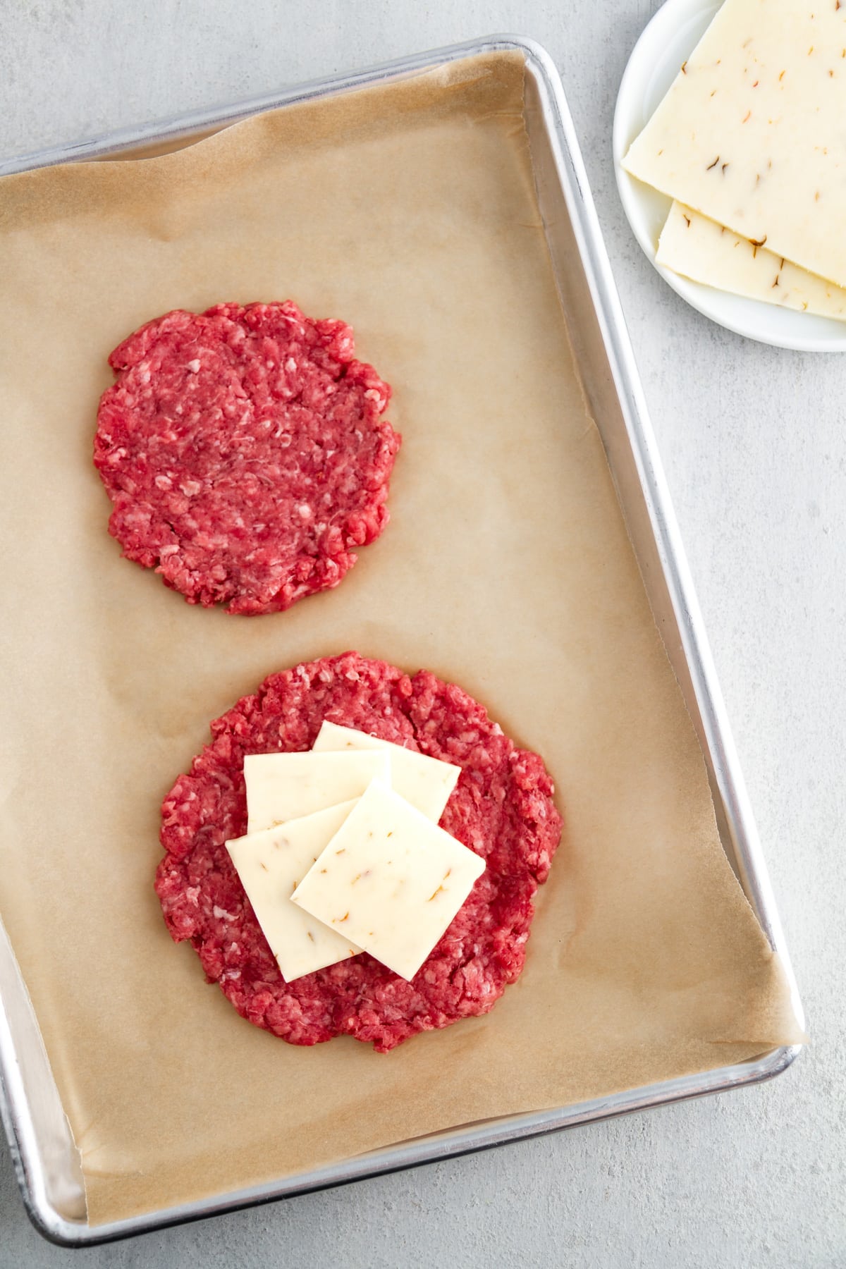 two hamburger patties and cheese slices on a baking sheet