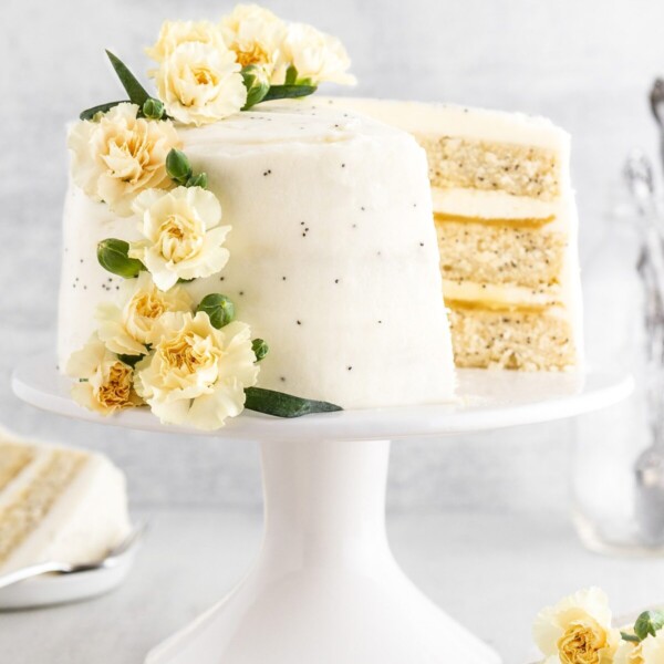 A lemon poppy seed cake on a cake stand with a slice taken out.
