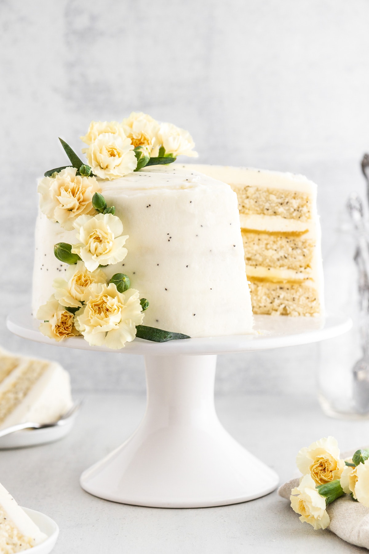 A lemon poppy seed cake on a cake stand with a slice taken out.