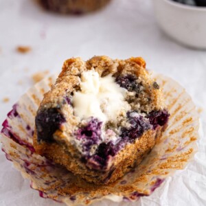 half of a sourdough blueberry muffin with butter on parchment paper.
