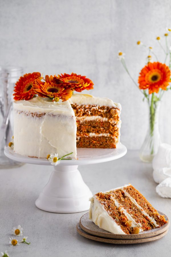 carrot cake on a cake stand with a slice on a plate off to the side