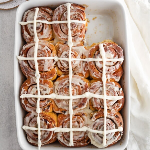 overhead of hot cross cinnamon rolls in a baking pan with one taken out.