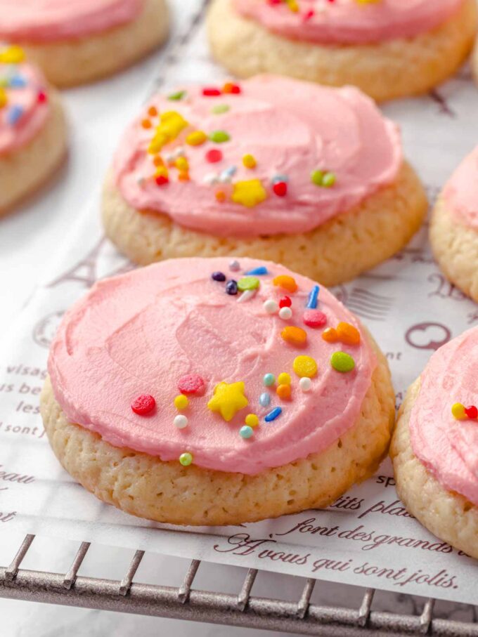 pink frosted sugar cookies with sprinkles on wire rack.