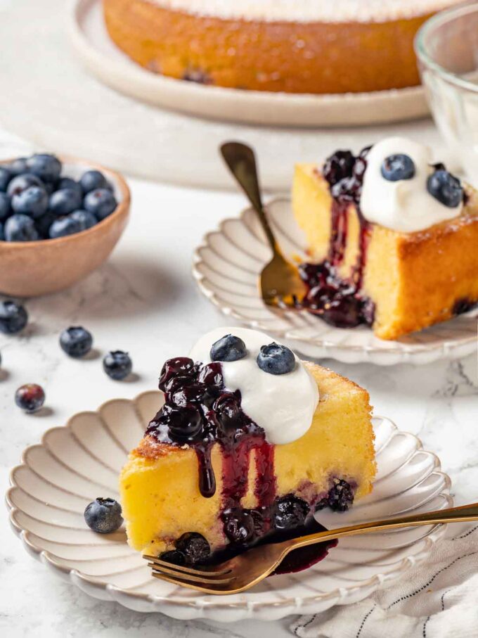 two slices ricotta blueberry cake with sauce and whipped cream.